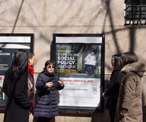Four women stand in front of a poster advertising an event about social policy in China.