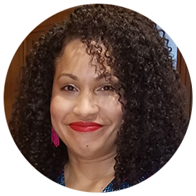 Erica smiles into the camera wearing rose colored lipstick and earrings. Her hair is cascades down her face in a tight wavy pattern.