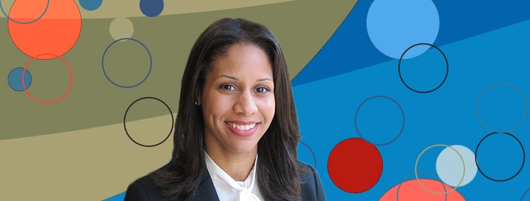 Dr. Alcantara wears a dark blazer while smiling and standing in front of a multi colored backdrop 