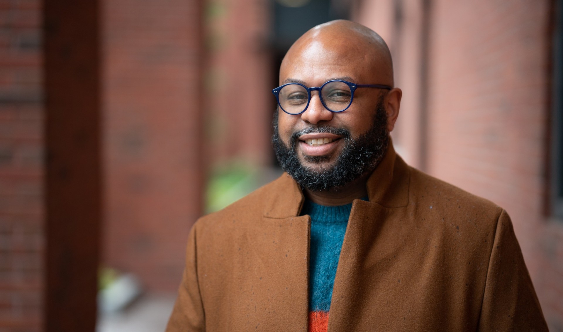 Photo of Desmond Patton in a brown blazer and blue and orange sweater.