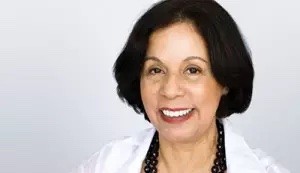 Dr. Cabrera smiles into camear wearing a dark blouse and white blazer.