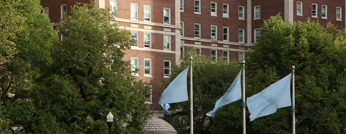 Exterior of campus housing building featuring columbia blue flags in front