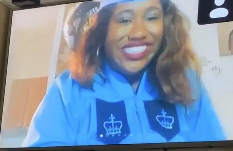 Alexis Perry smiles on screen dressed in a commencement robe