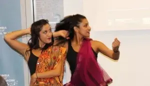 Two women dressed in asian pacific island clothings are in the midst of a  pose while wearing over the shoulder pashminas
