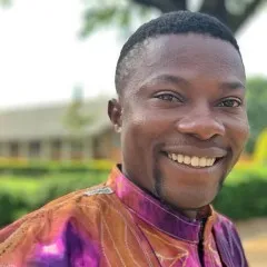 Bwema wears smiles at camera wearing a multi colored brown and fuschia shirt