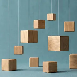 Wooden cubes are suspended in the air by transparent strings against a blue-grey wall