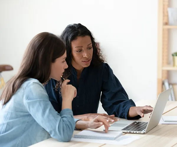 Two women look at a laptop as they talk.