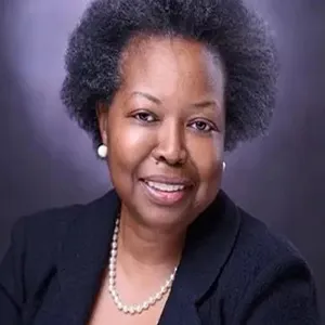 Dr. Allen wears a pair of pearl earrings and necklace. 
 She smiles into camera wearing a dark blazer.