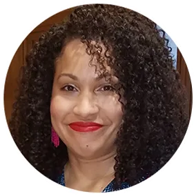 Erica smiles into the camera wearing rose colored lipstick and earrings.  Her hair is cascades down her face in a tight wavy pattern. 