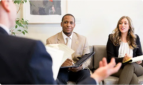 Two people in business suits sit across from a third person, also wearing a business suit