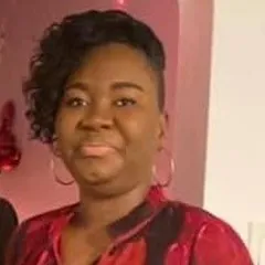 Lavenes smiles at camera wearin hooped earrings with a maroon and black multi colored blouse