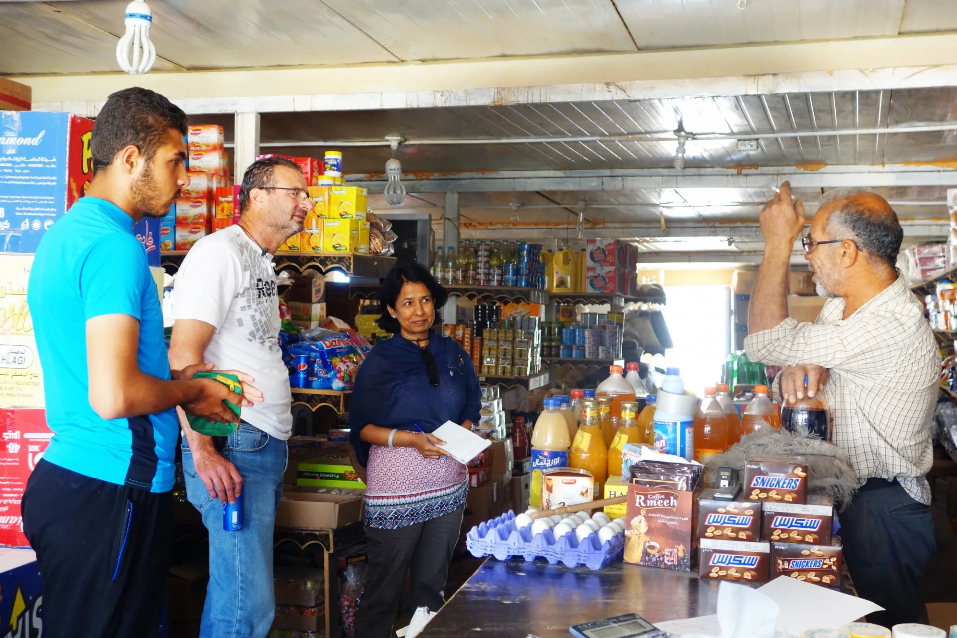 ASPIRE team visit a local market where goods of eggs and beverages are on the countertop while the team are in discussion with the male clerk behind the table.