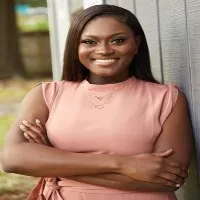 Regina smiles into camera wearing an apricot colored blouse. 