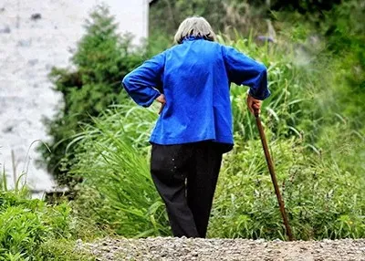 person walking with cane wears a royal blue blazer and black pants while taking a walk in woods 