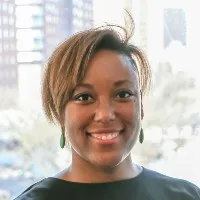 Professor Courtney Cogburn smiles into camera wearing a dark crewneck top 
