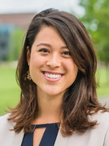 Tori Guen smiles at camera wearing parted brown hair.  Her blouse is beige blouse atop of a navy blue blouse.