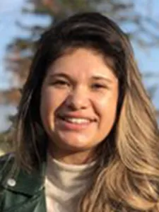 Yajaira smiles into camera she wears a beight colored turttle neck and black leather jacket. 