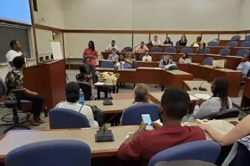 Classroom filled with students are seated while listening to a lecturer.