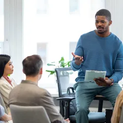 Instructor is seated while speaking to a room of adult students  