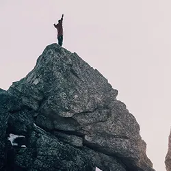 a man stands atop a mountain while arms are open wide 
