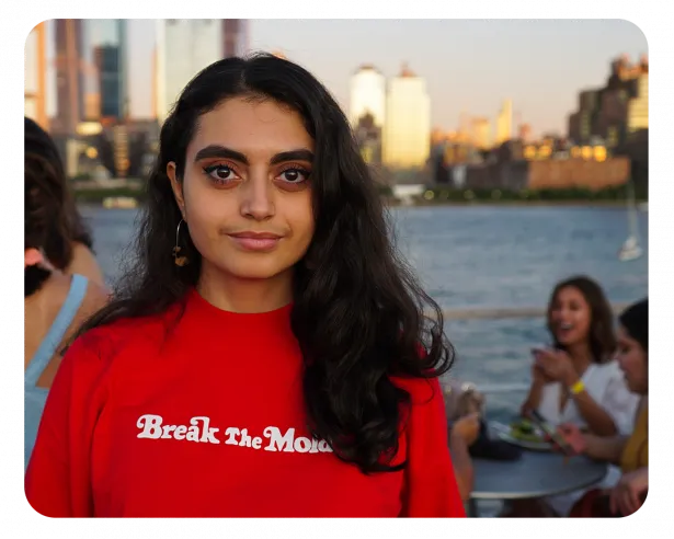 Isanbel stands with dark hair wearing a red sweatshirt with white lettering. 