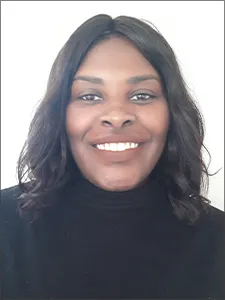 Joya weas a dark colored turtleneck and smiles into camera.  She wears her hair with a center part and flowing tresses alongside her face.