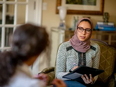 woman wearing a hijab wears a zip down while taking notes from another woman wearing a pony tail