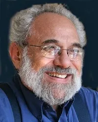 Mr. Friedman wears a blue collared button down shirt and suspenders.  He wire framed eyeglasses and smiles. 